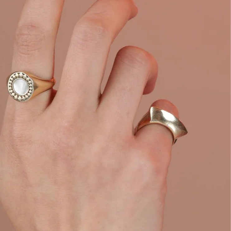 Hand wearing two rings on a beige background