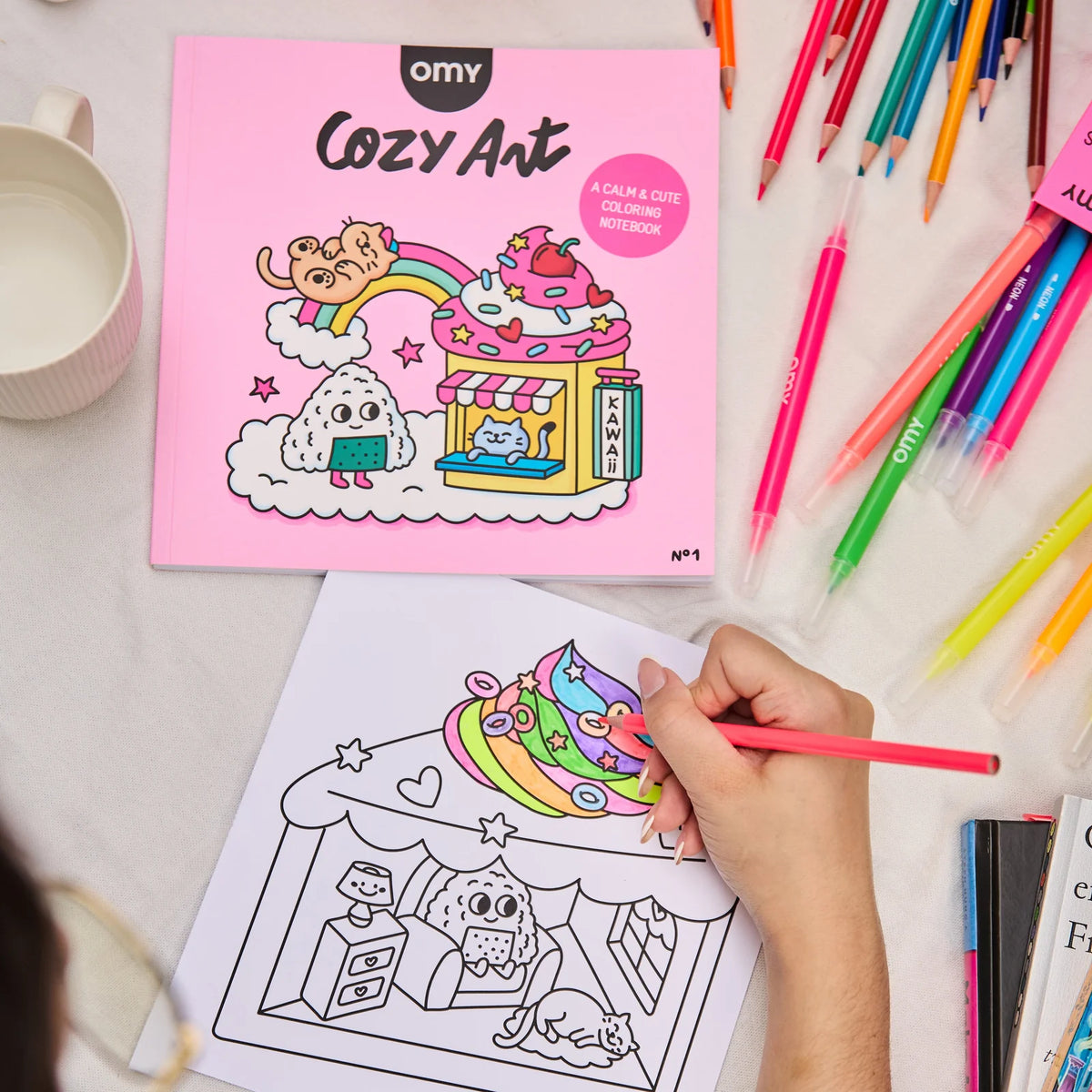 Coloring notebook titled 'Cozy Art' by OMY with cartoon illustrations on a pink cover.