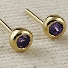 Gold stud earrings with purple gemstones on a light wooden background