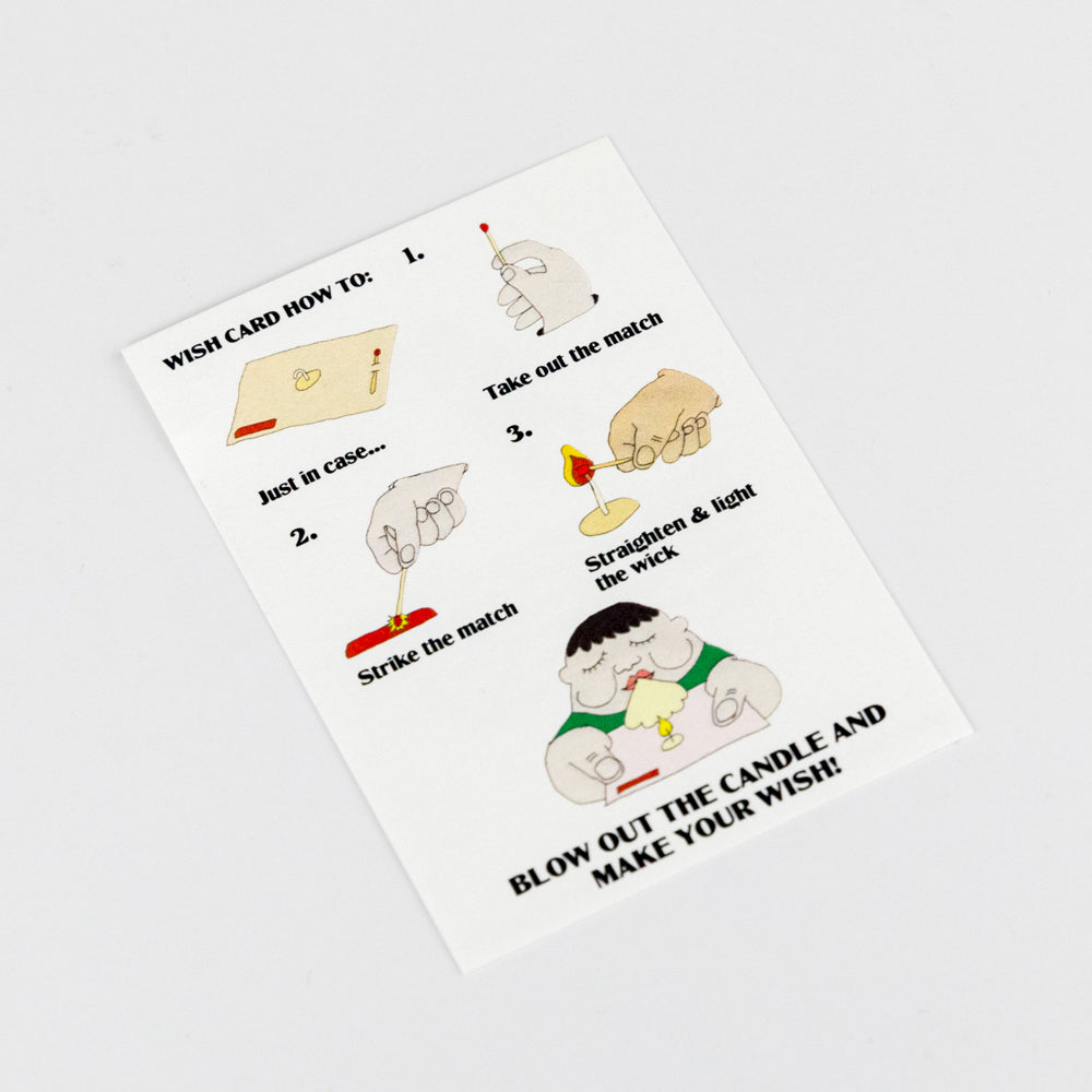 A greeting card with a red heart shape and a white background, featuring a match, a strike-pad, and a candlewick. The text 'One Wish' is printed on the card.