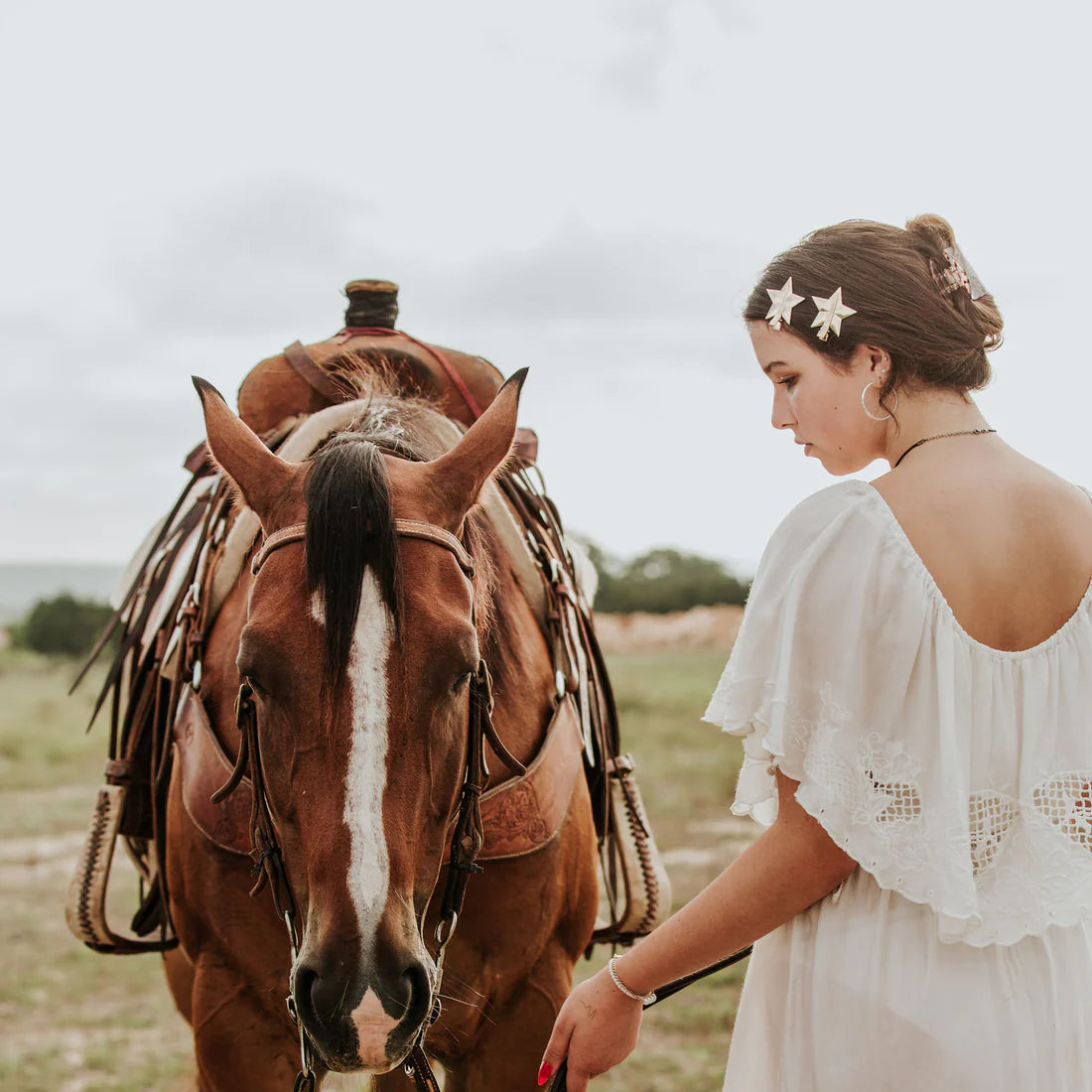 Woman in a white dress standing next to a horse in an open field