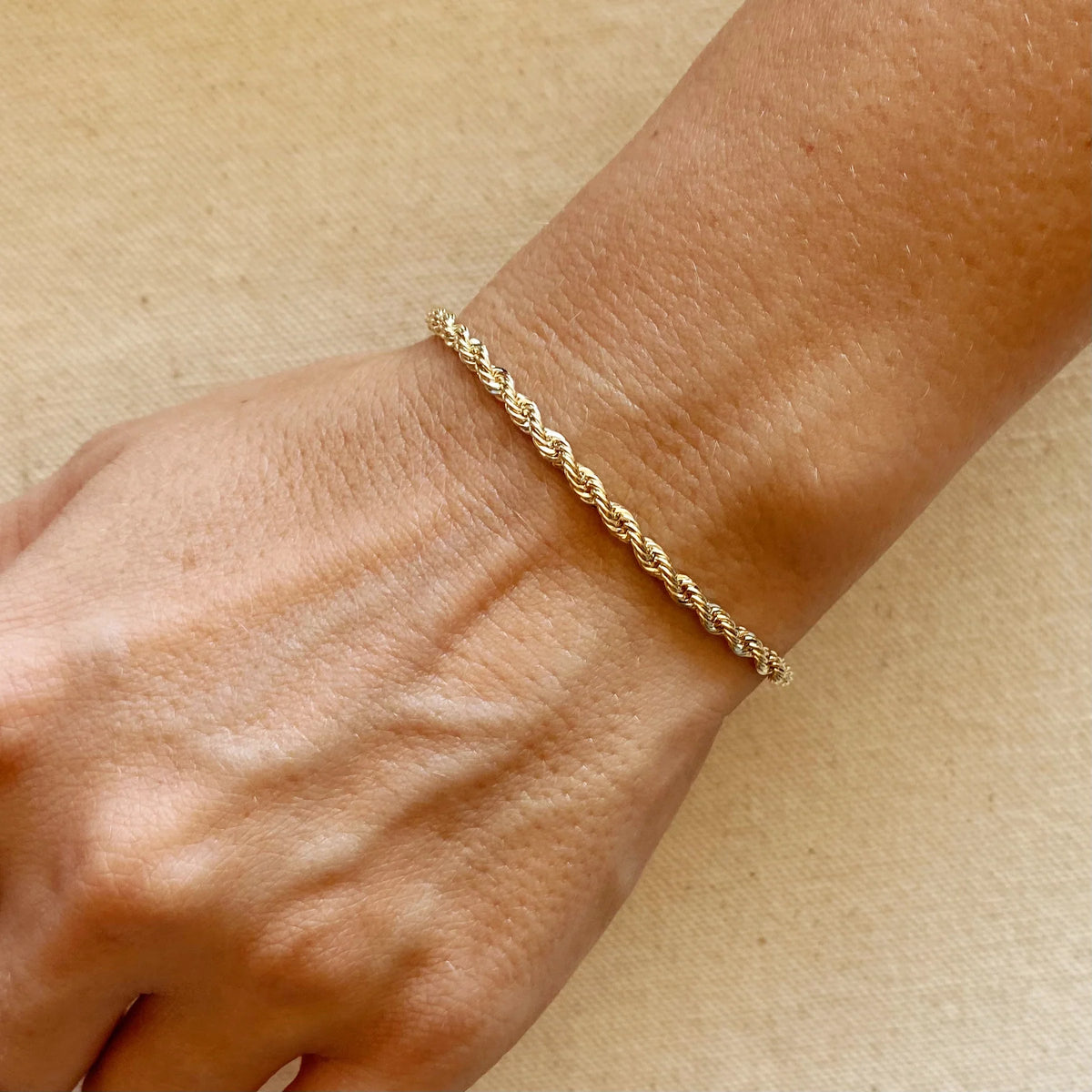 Gold bracelet on a wrist against a beige background
