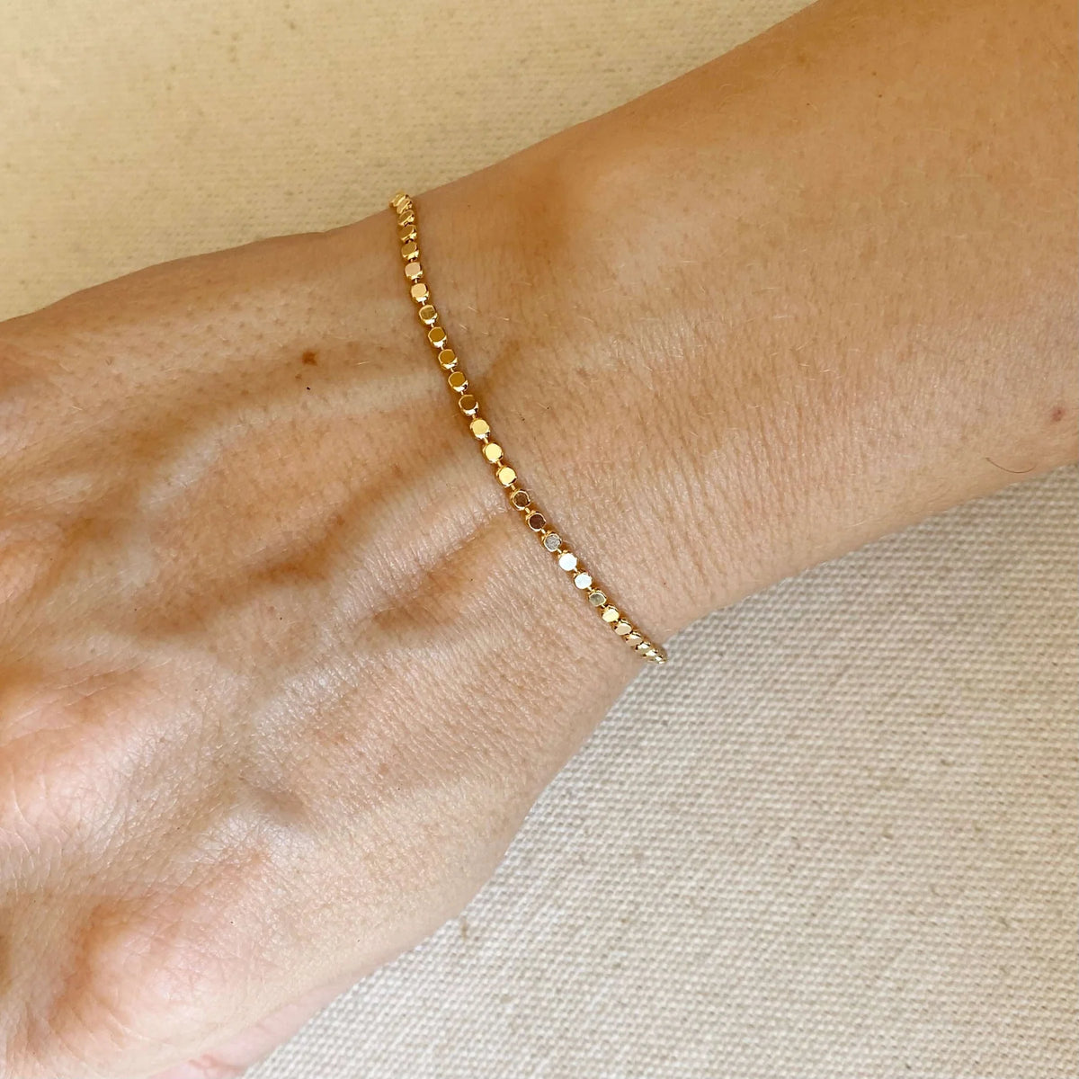 Gold bracelet on a wrist against a neutral background